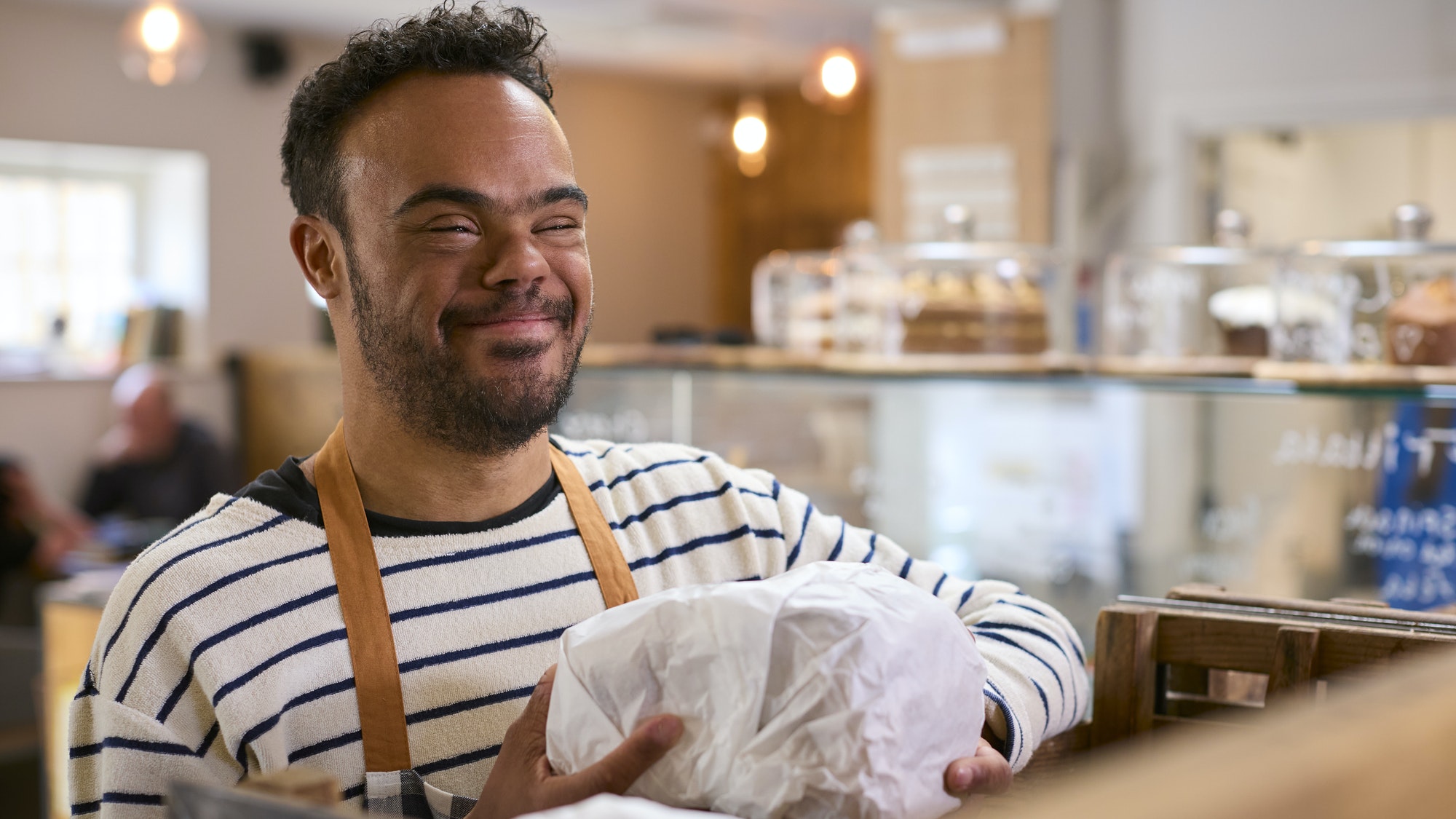 Smiling Man With Down Syndrome Stocking Shelf With Bread In Food Shop