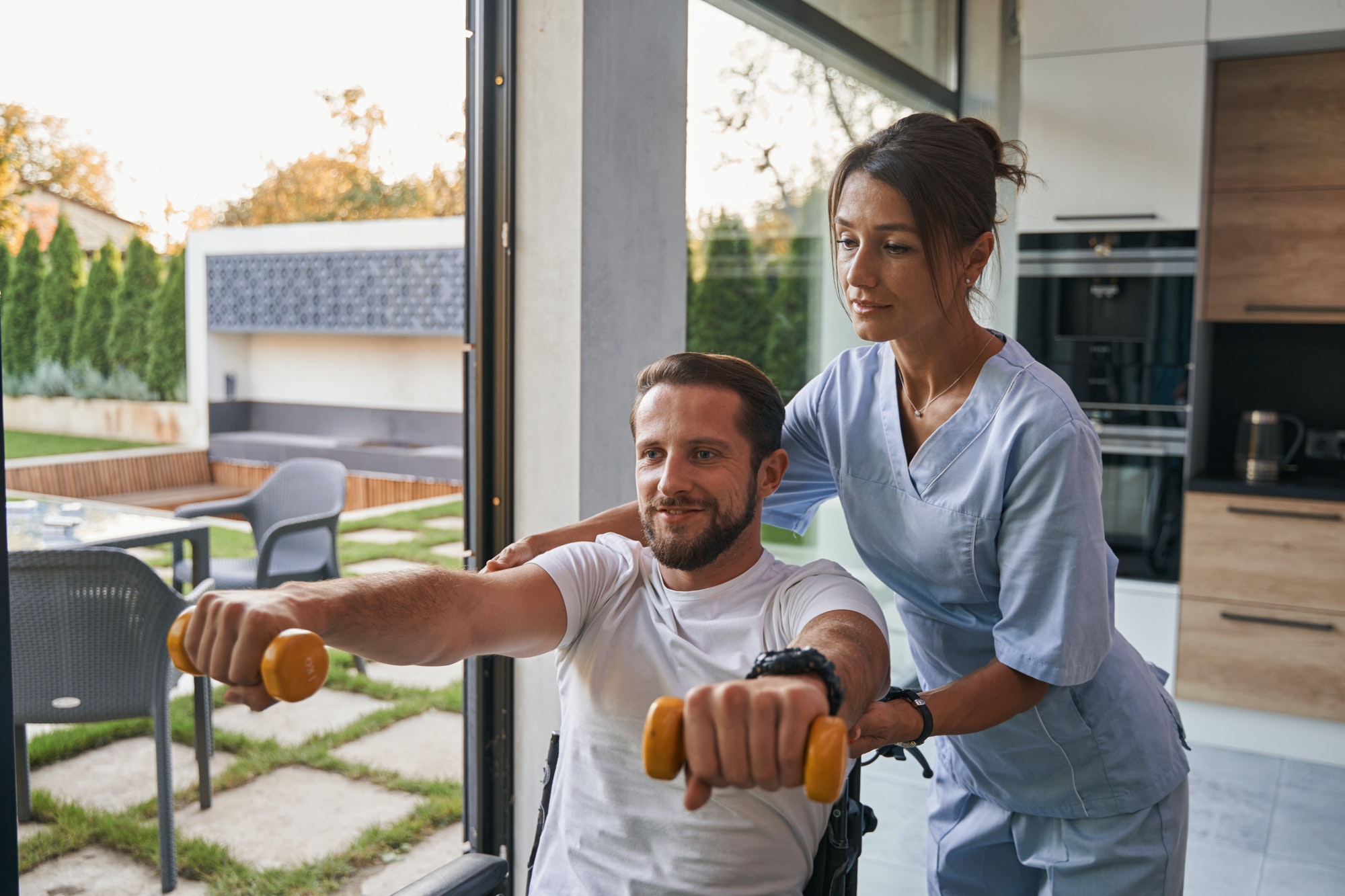 Woman physiotherapist helping to the man patient with physical disability in his house