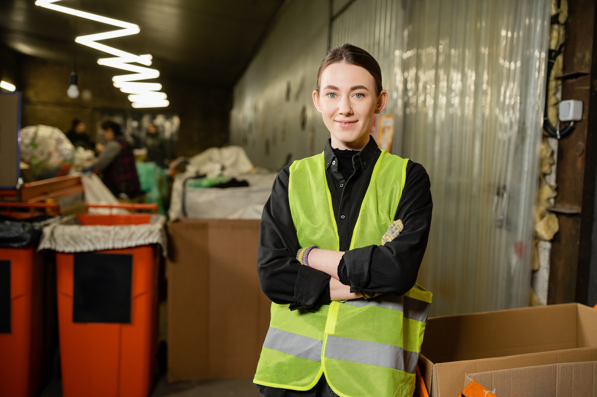 Young and smiling worker of waste disposal station in high visibility vest looking at camera and